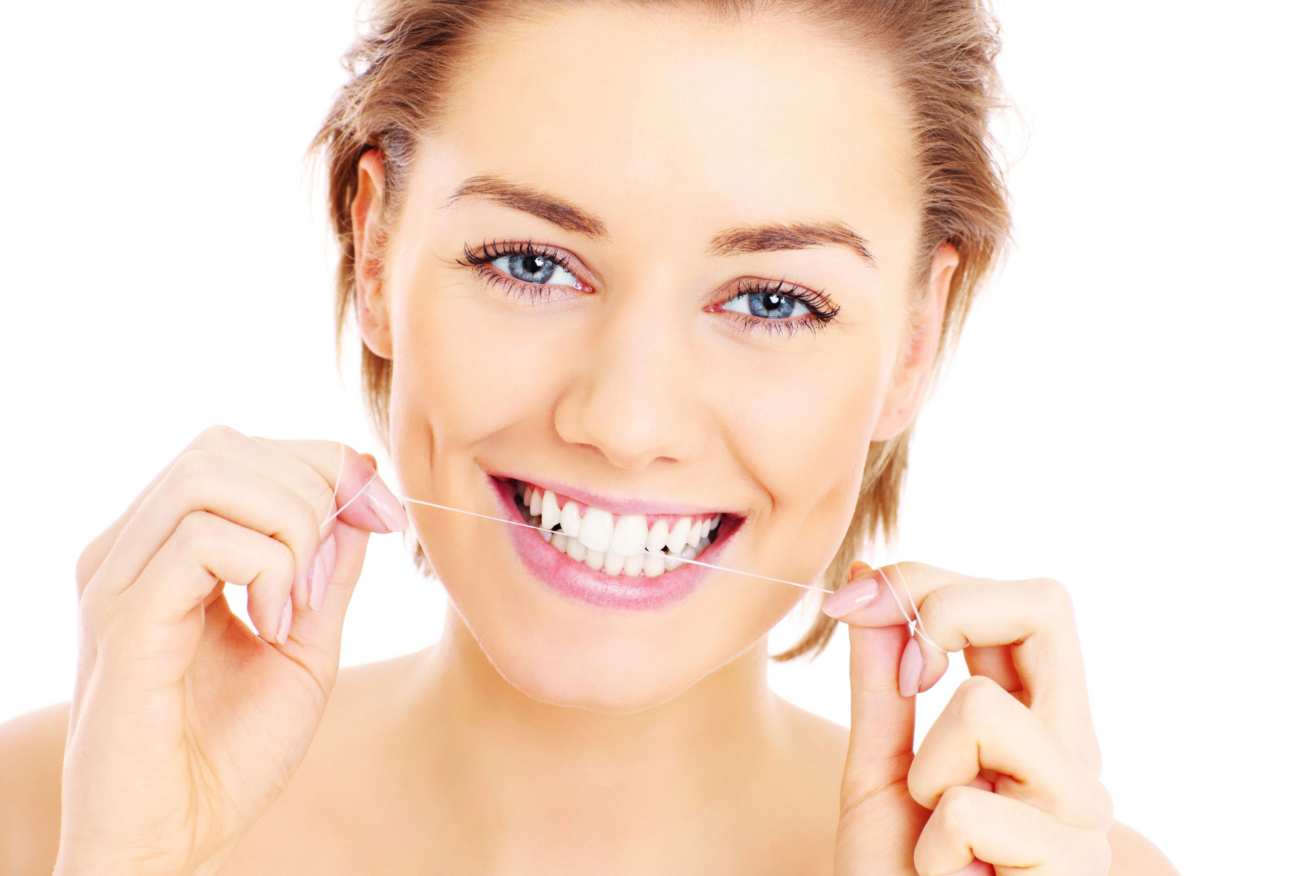 A woman smiling while gently flossing her teeth with dental floss.