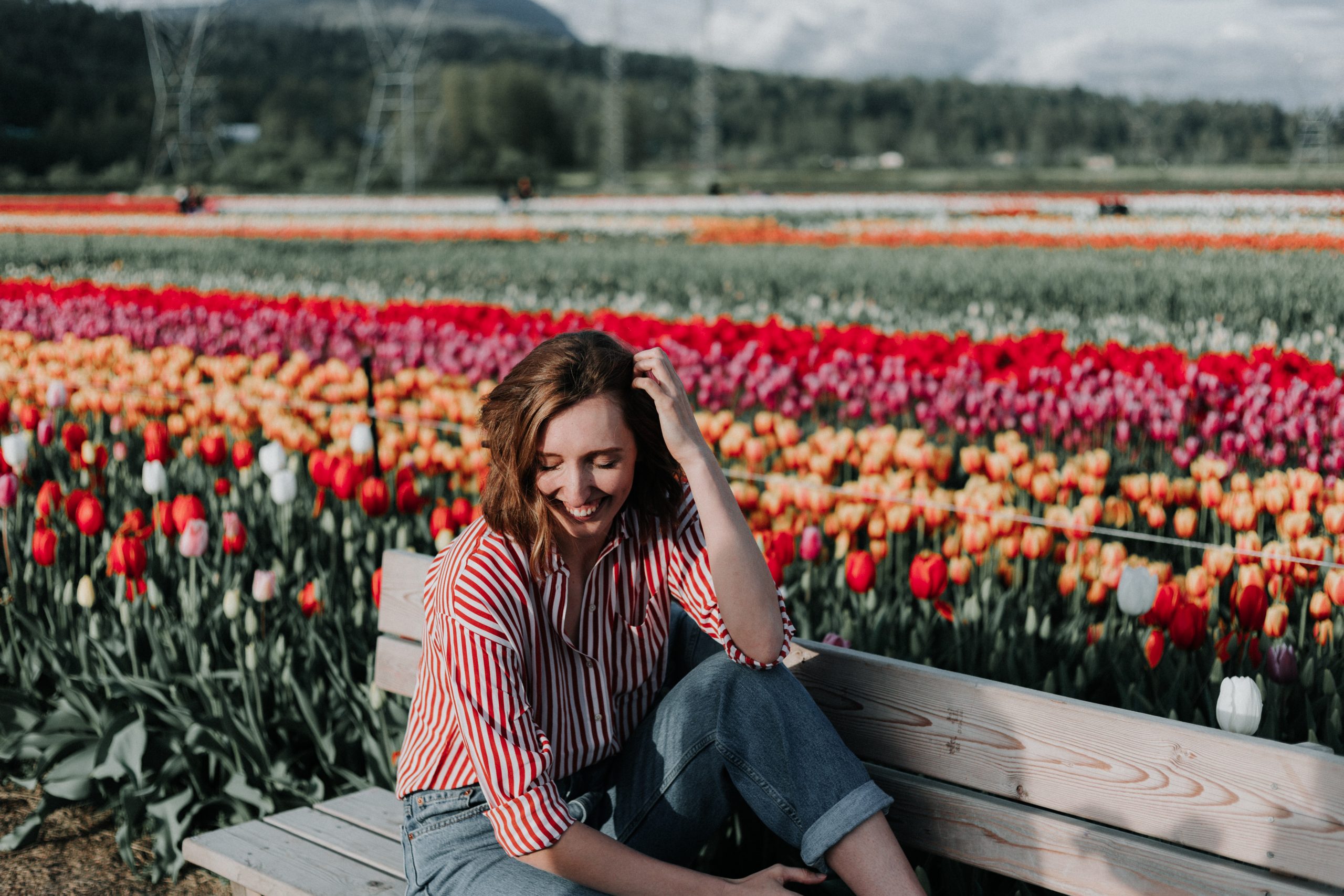 A young woman laughing while sitting on a bench, surrounded by colorful tulip fields.