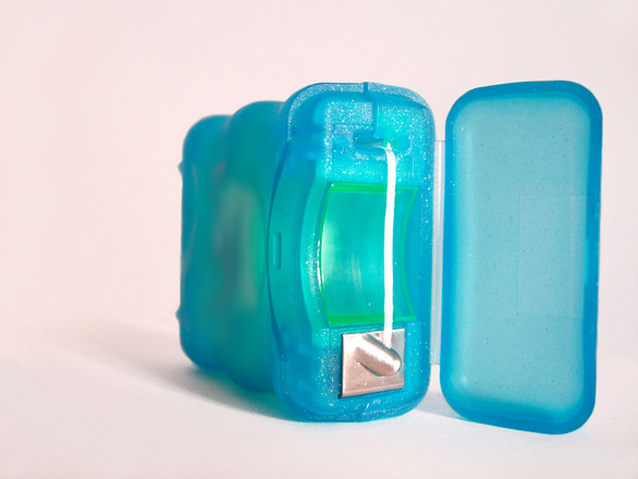 A blue dental floss container opened to reveal the floss inside.