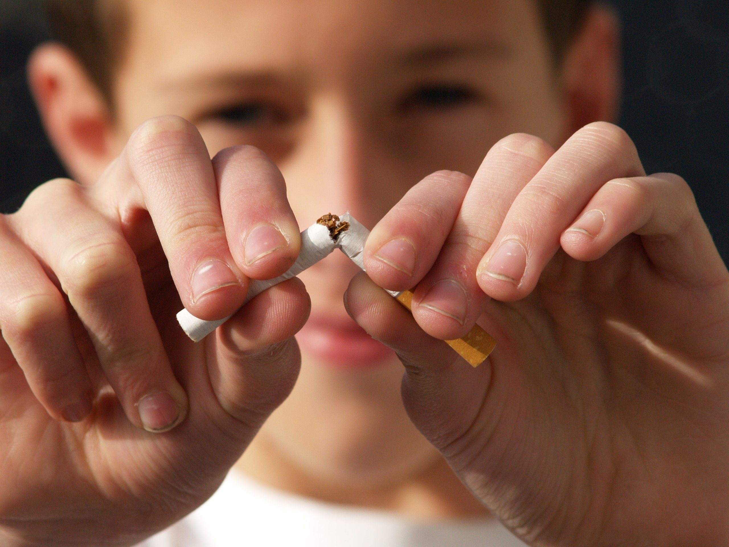 A child is breaking a cigarette in half with both hands, showing a determined expression.