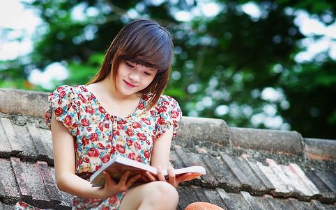A young woman sitting on a rooftop, reading a book, surrounded by greenery.