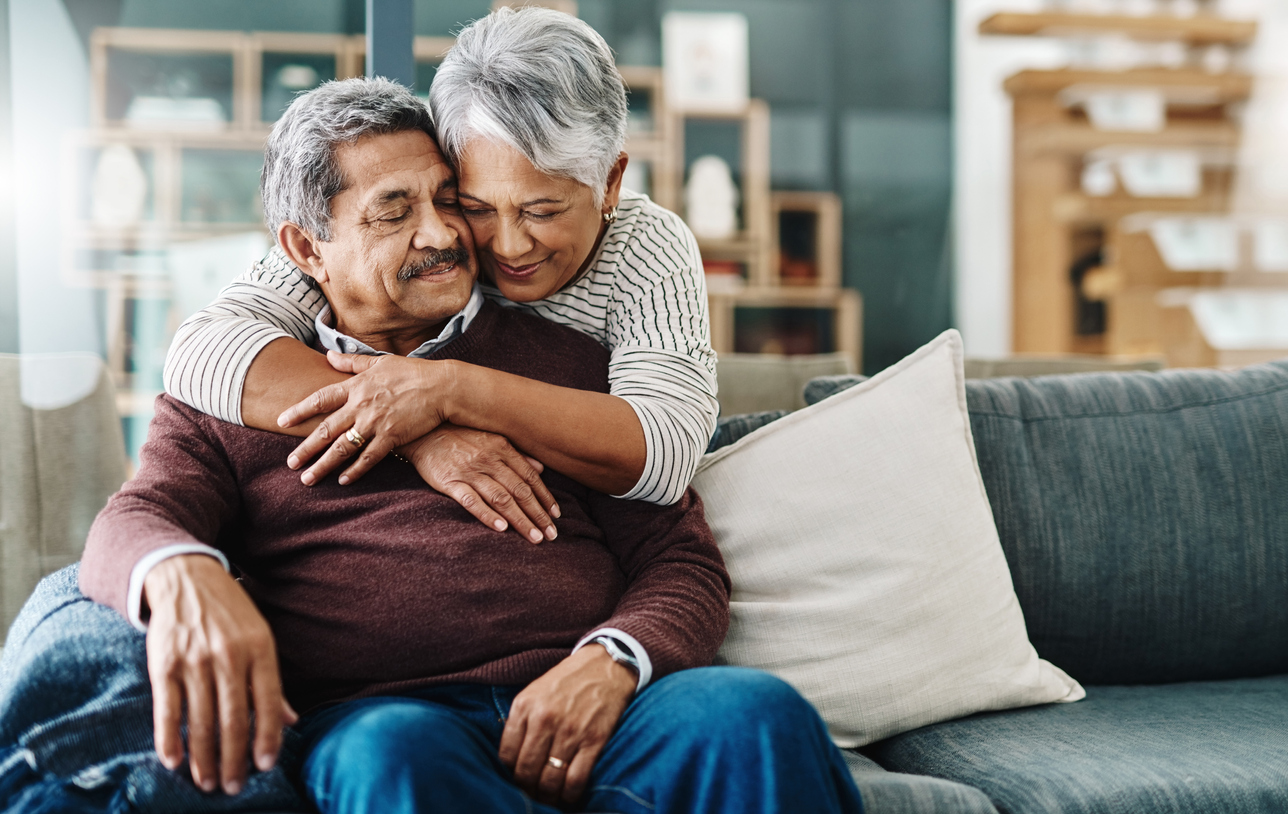 A joyful older couple embracing on a comfortable sofa in a cozy living space.