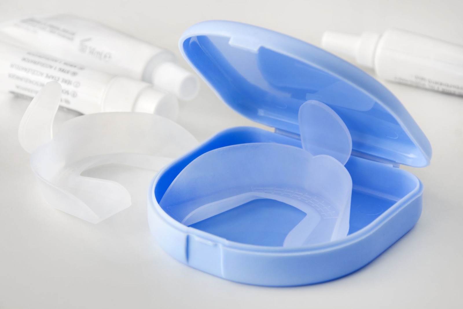 A blue dental retainer case with a clear retainer inside, surrounded by dental tubes and tools.