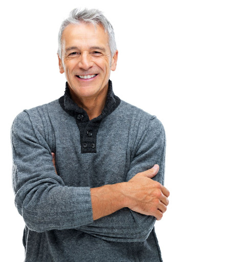 A smiling older man with gray hair wearing a gray sweater, standing with arms crossed against a white background.